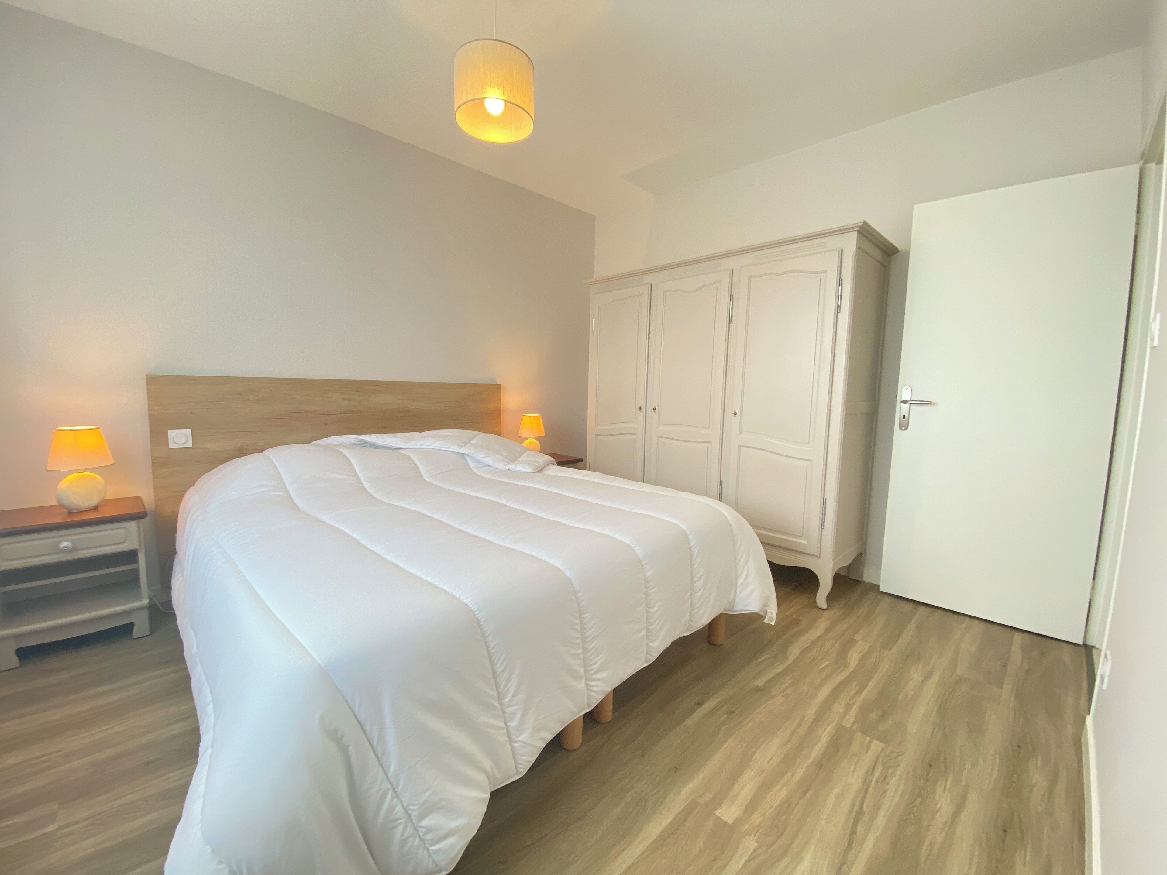A bedroom with a large bed, two bedside lamps, a wardrobe, and a ceiling light.