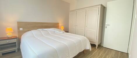 A bedroom with a large bed, two bedside lamps, a wardrobe, and a ceiling light.