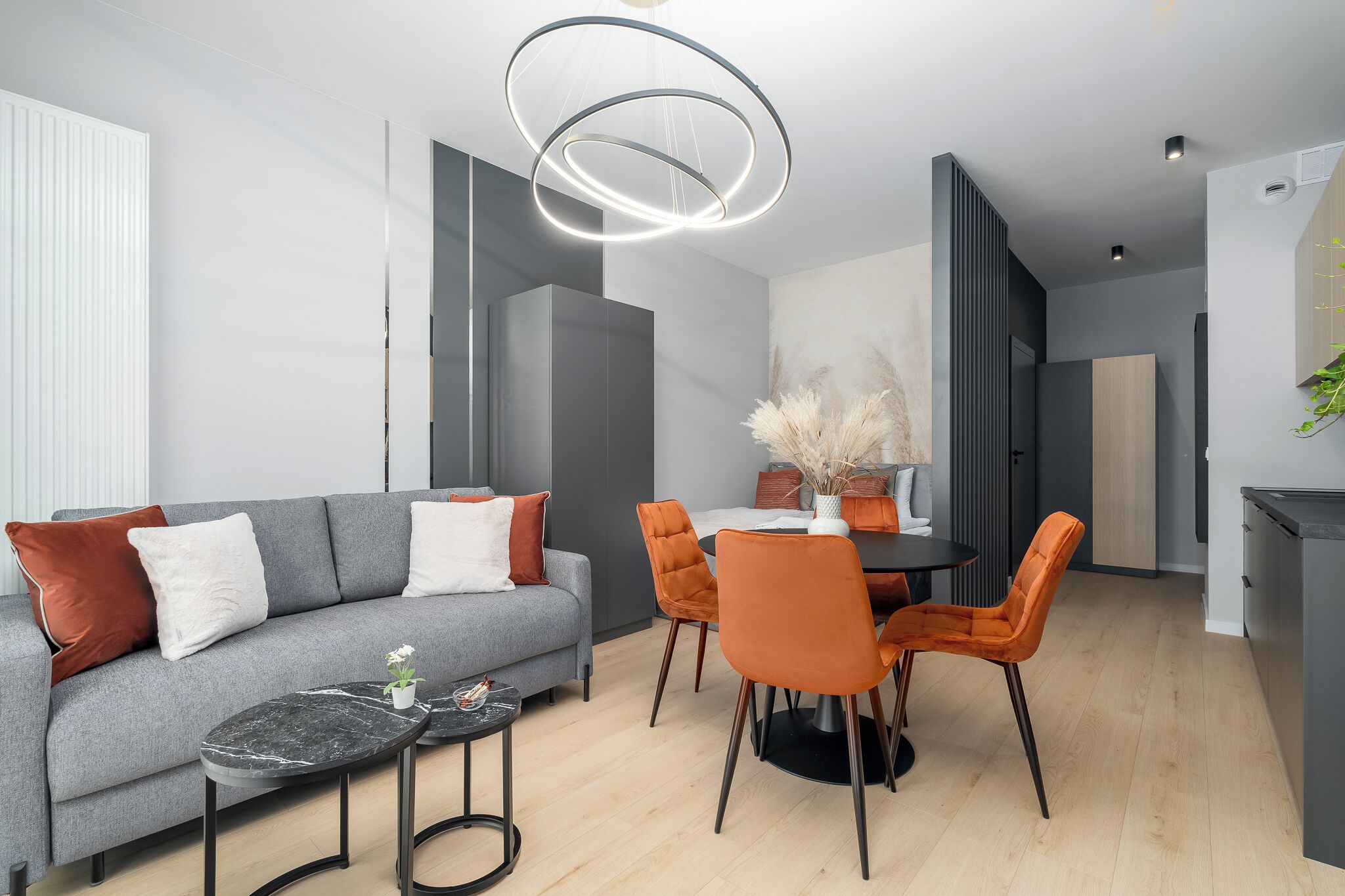 A modern living room with a grey sofa, orange chairs, a dining table, and a black marble coffee table.