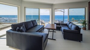 A modern living room with large windows, a black leather sofa, a wooden coffee table, and a view of the ocean. - at SUNSET VILLA INAMI (印南町)