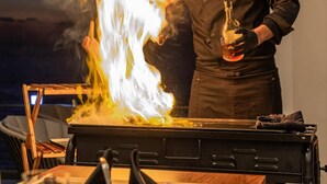A chef performing a flambé with a bottle on a stove in a kitchen. - at SUNSET VILLA INAMI (印南町)