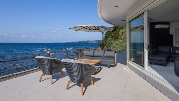 A modern outdoor patio with a view of the sea, featuring a sofa, chairs, and a table. - at SUNSET VILLA INAMI (印南町)