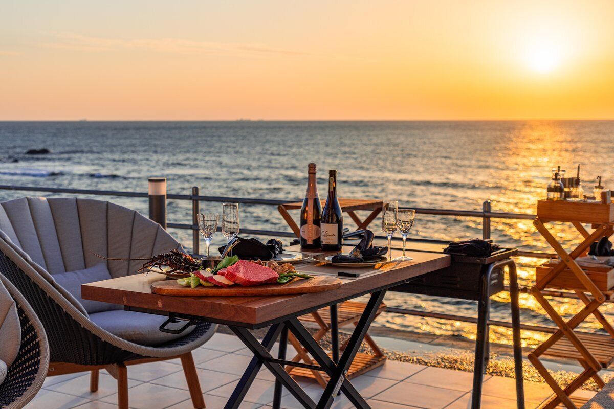 A dining table with a lobster, wine, and glasses, set against a sunset view.