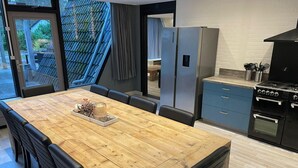 Een moderne keuken met een houten eettafel, zwarte stoelen, een koelkast en een fornuis.