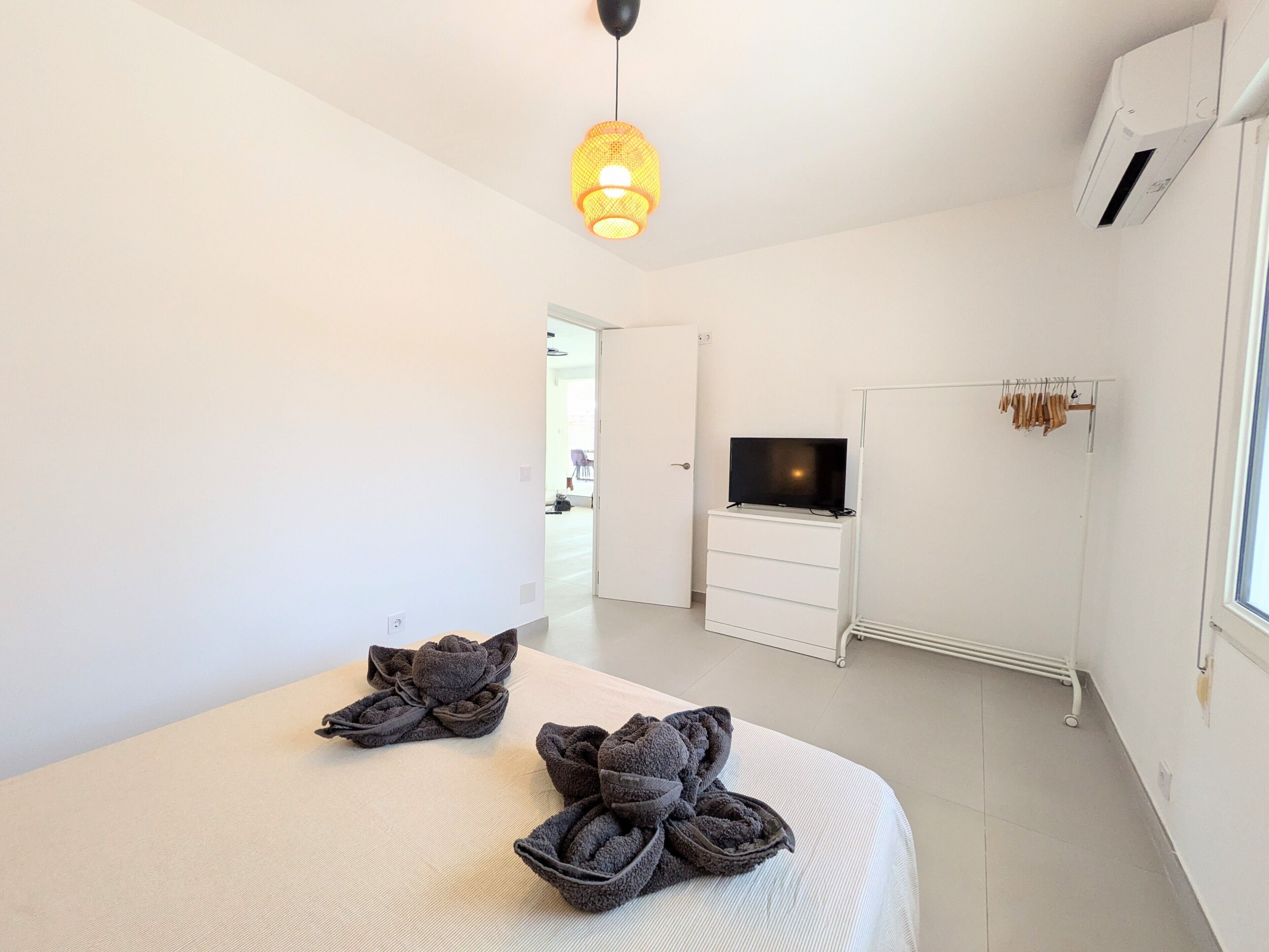 Un dormitorio con una cama, un televisor sobre una cómoda, un radiador y un perchero.