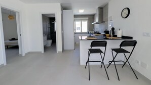 Cocina moderna con una isla central, dos taburetes de bar, un reloj y baño a la vista.