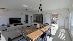 Una sala de estar moderna con sofá, televisor, mesa de comedor de madera y una cocina visible a través de un arco.