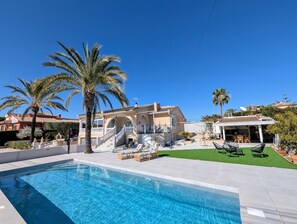 A pool area with a house, palm trees, and outdoor furniture. - Holiday Home 'R-70 Vacacional' with Private Pool, Wi-Fi, and Air Conditioning (Ciudad Quesada)