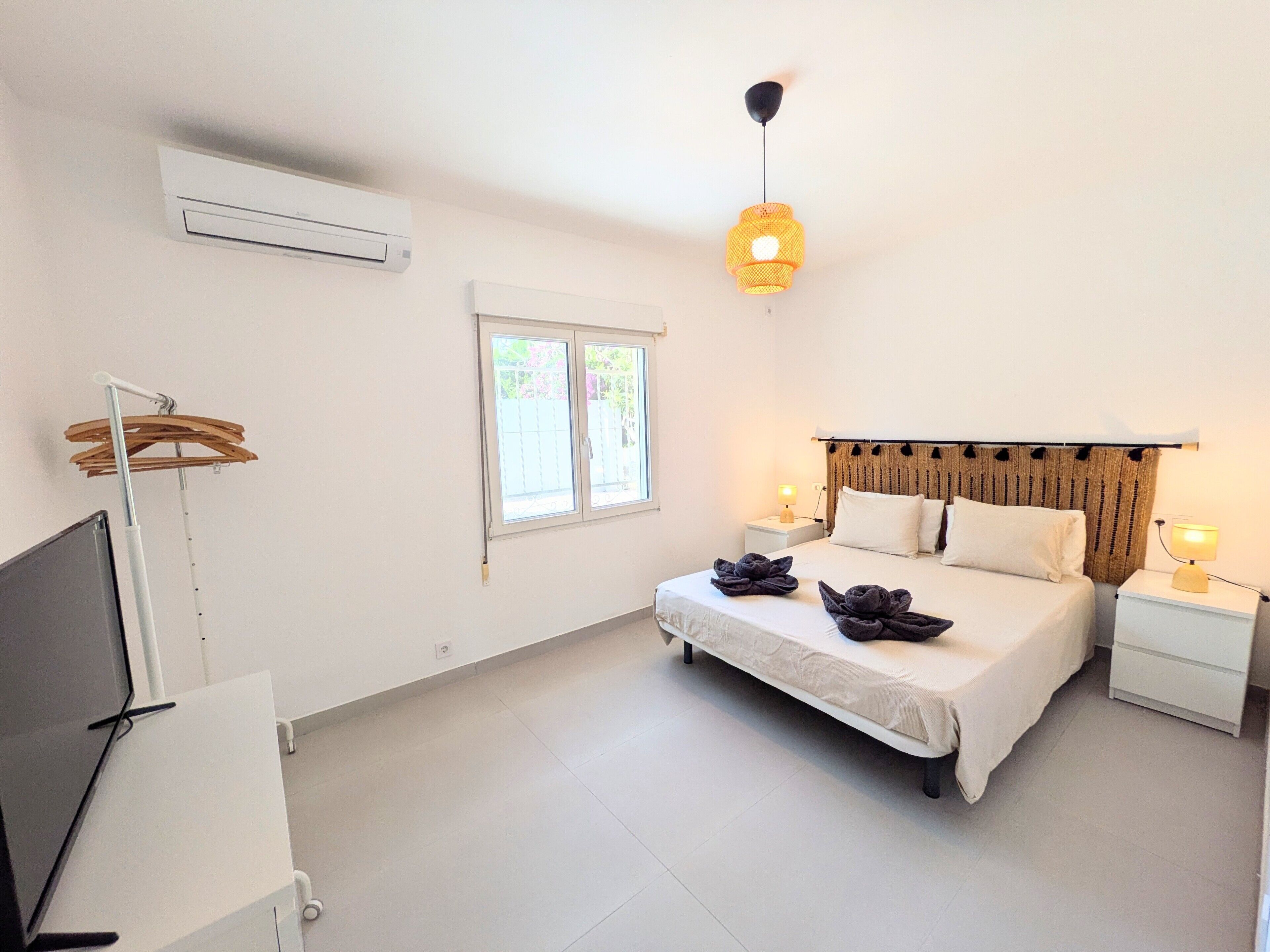 Een slaapkamer met een bed, bedlampen, een televisie, een airconditioner en een raam.