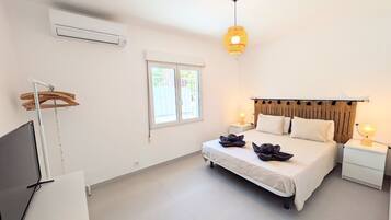 Een slaapkamer met een bed, bedlampen, een televisie, een airconditioner en een raam.