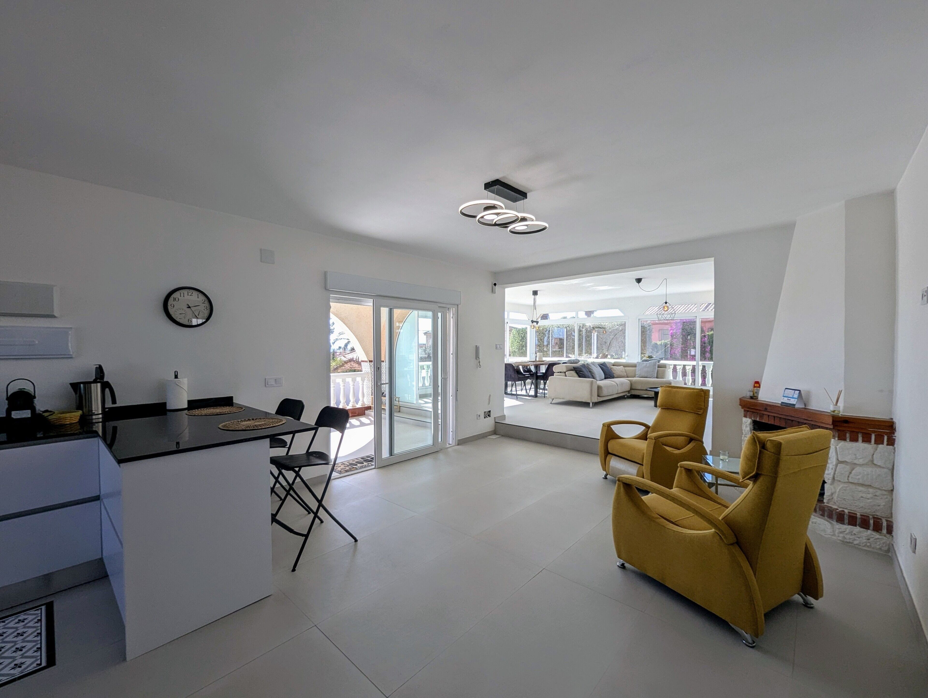 A modern kitchen with a dining area, a yellow armchair, and a view of the outside.