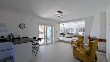 A modern kitchen with a dining area, a yellow armchair, and a view of the outside.