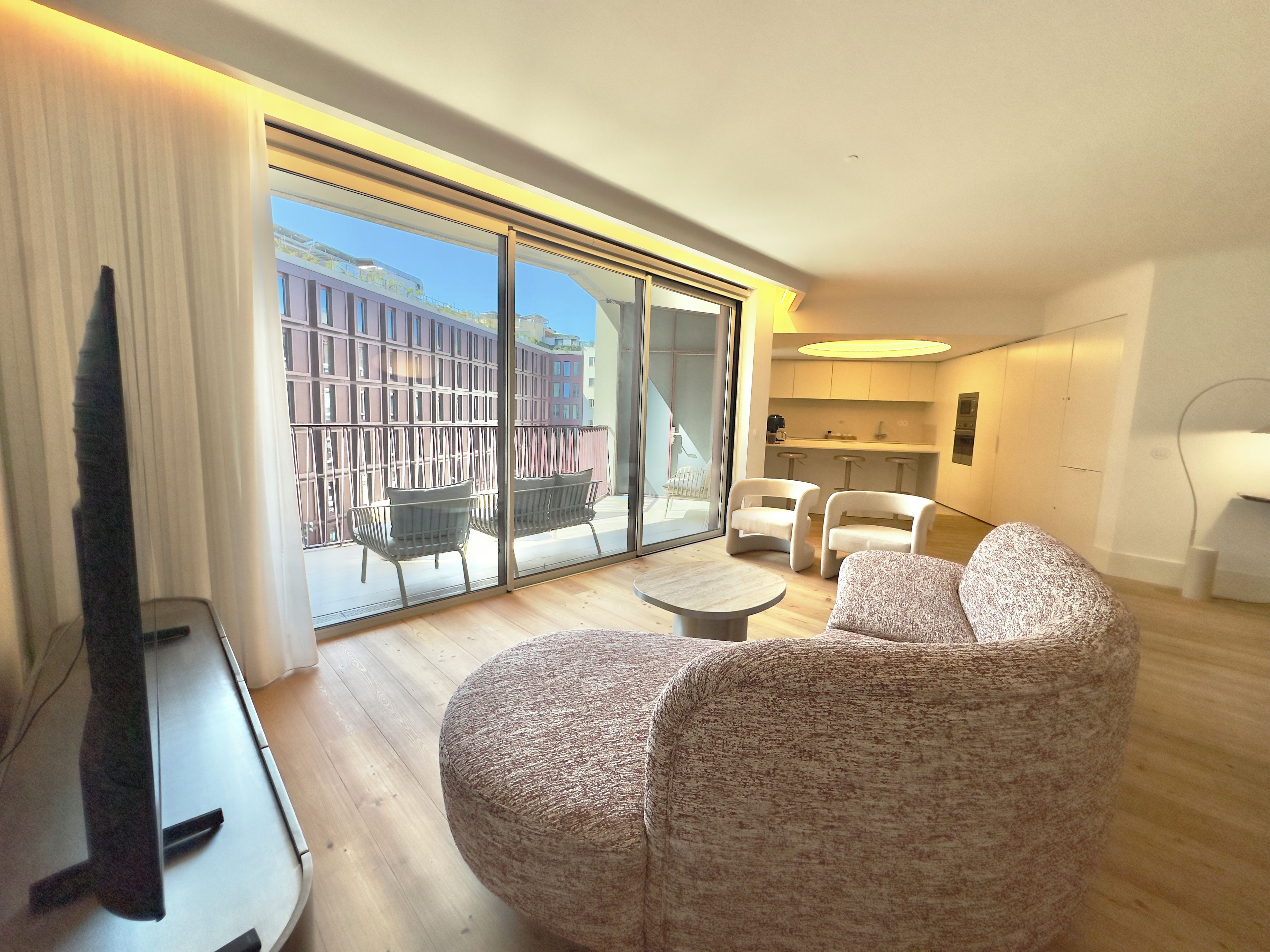 A modern living room with a large sliding glass door leading to an outdoor balcony, a flat-screen TV, and a small round table.