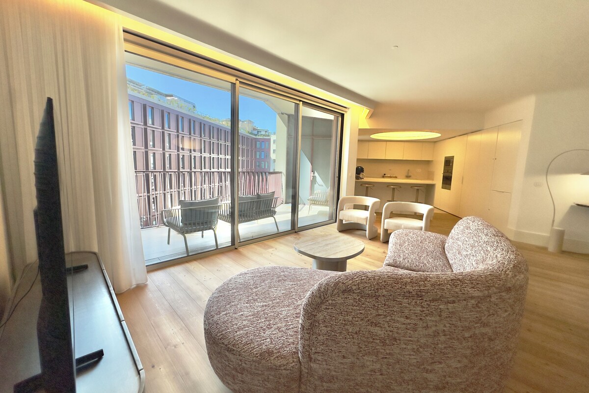 A modern living room with a flat-screen TV, a round coffee table, and two patterned sofas.