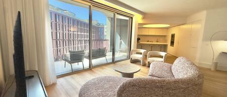 A modern living room with a large sliding glass door leading to an outdoor balcony, a flat-screen TV, and a small round table.