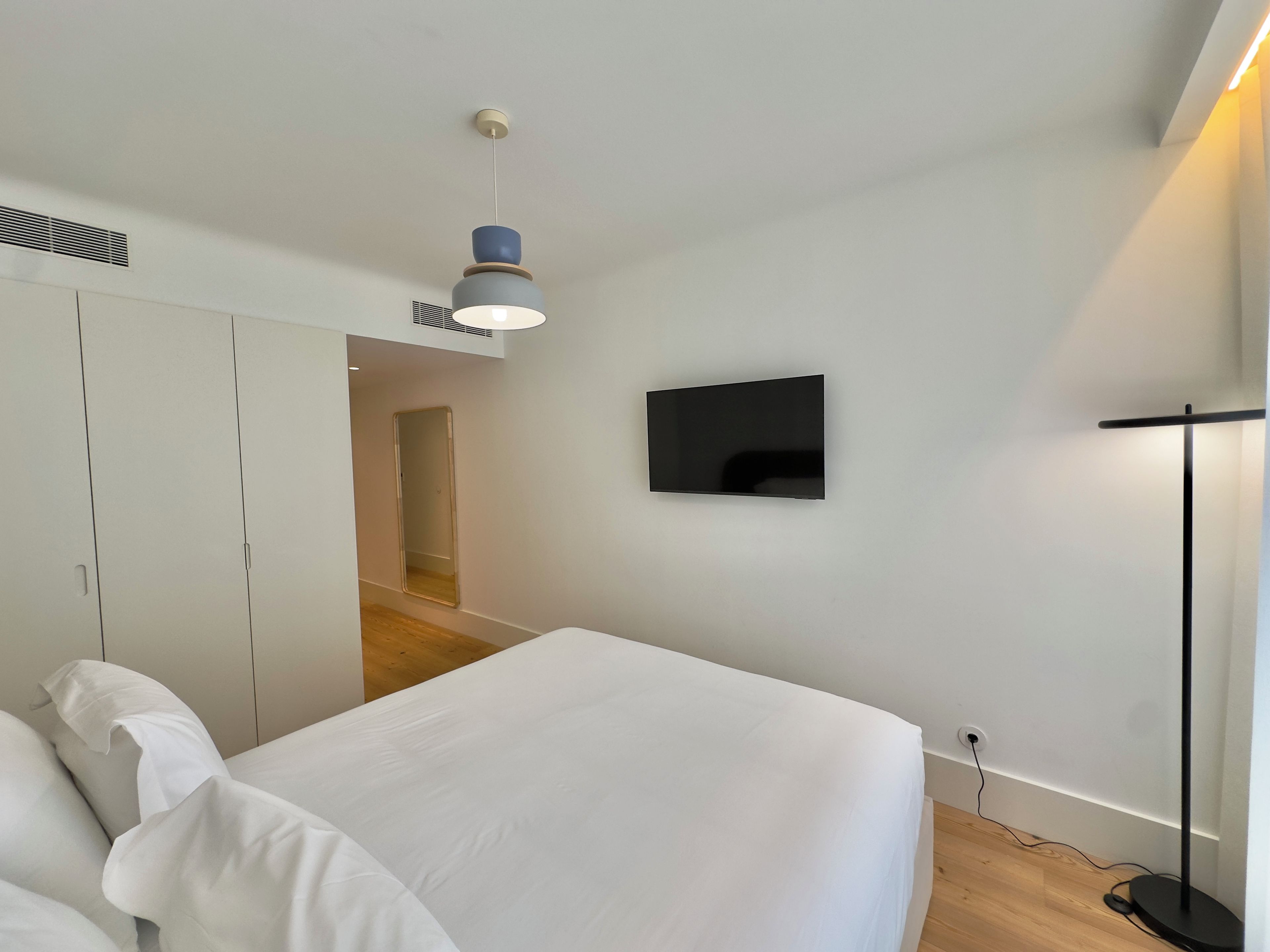 Ein modernes Schlafzimmer mit einem Bett, einem flachbildfernseher an der Wand und einer Deckenleuchte.
