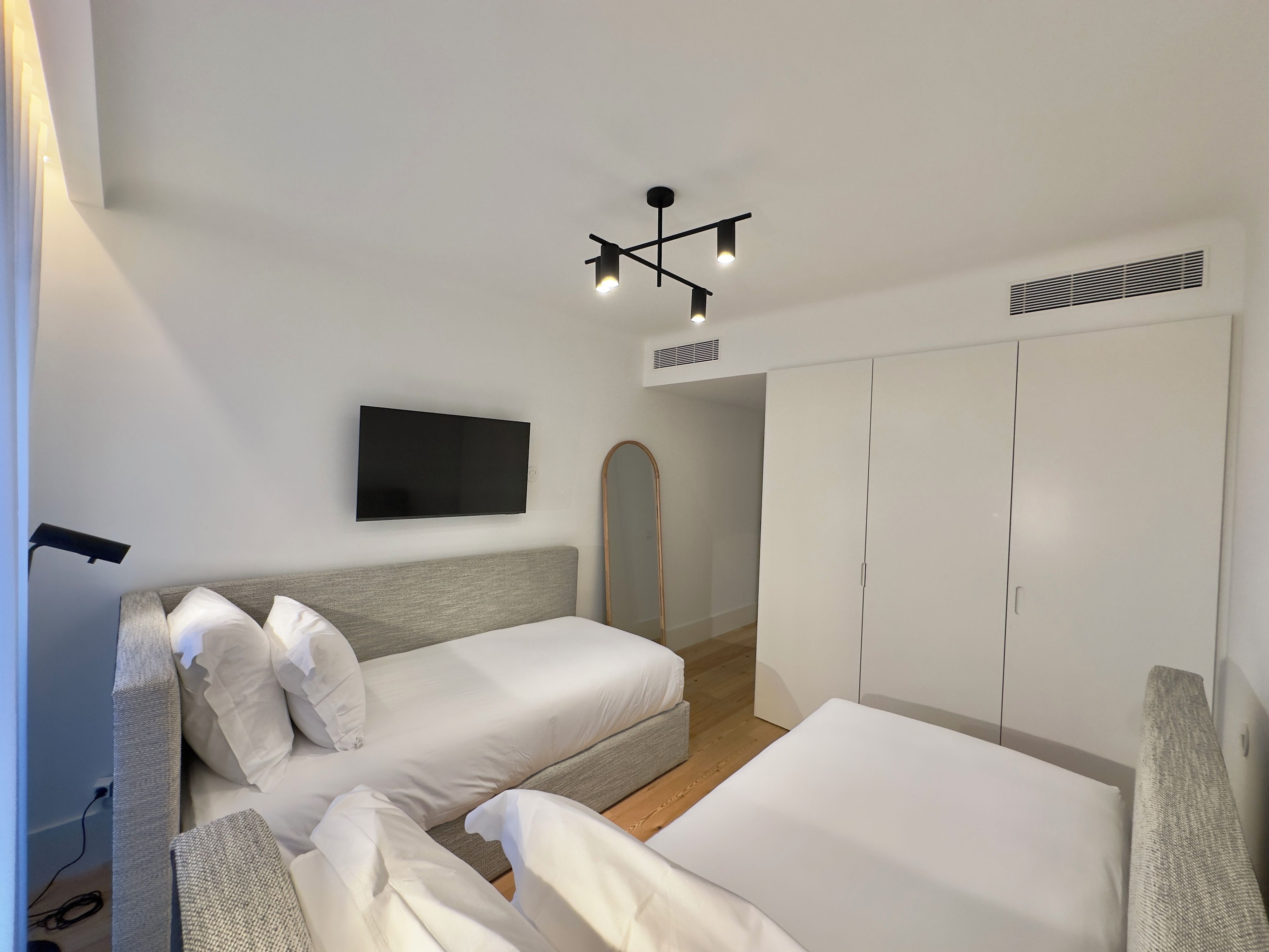 A bedroom with two beds, a TV, a wardrobe, and a ceiling light fixture.