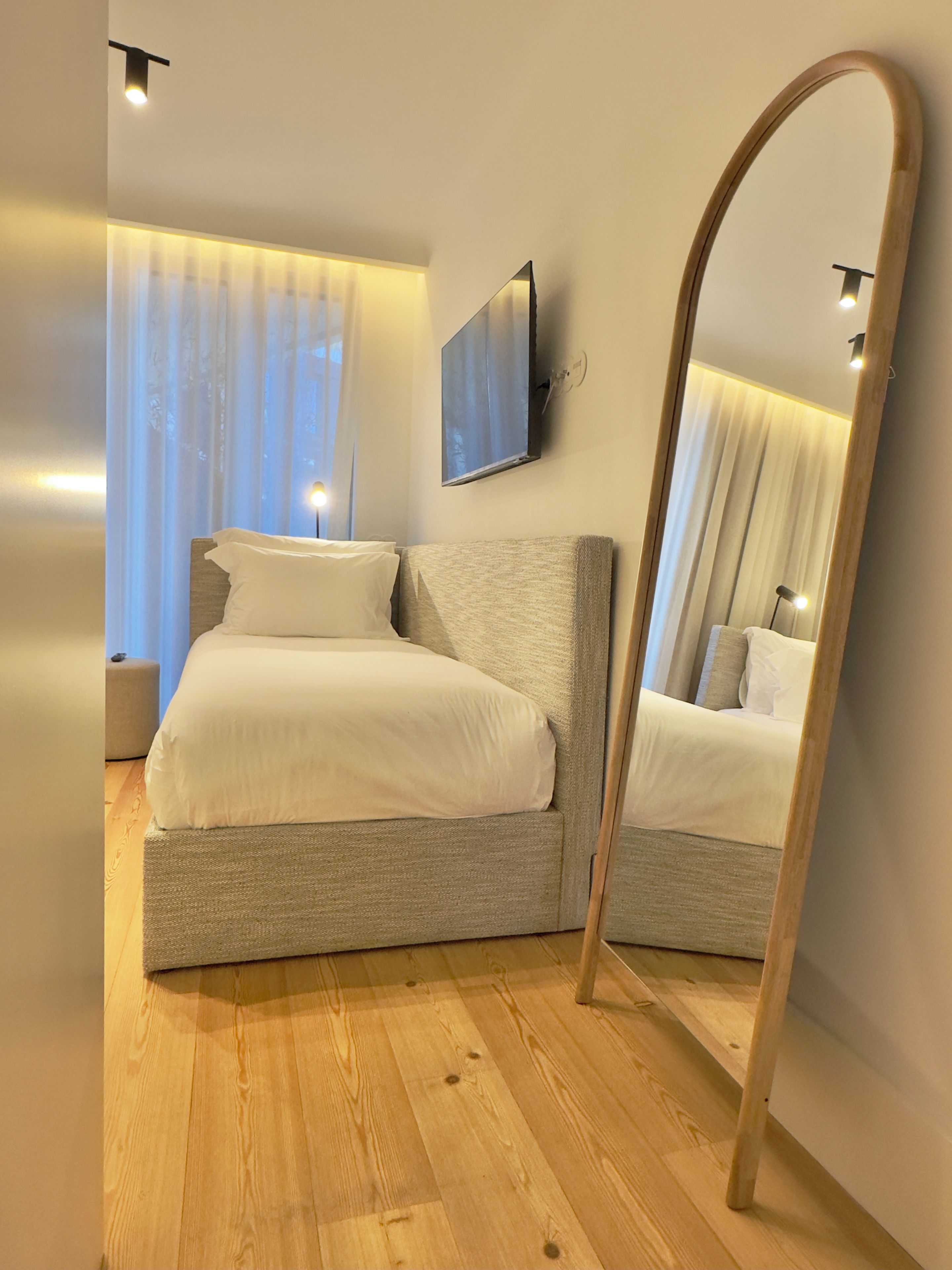 A bedroom with a bed, a mirror, a television, and a window with curtains.