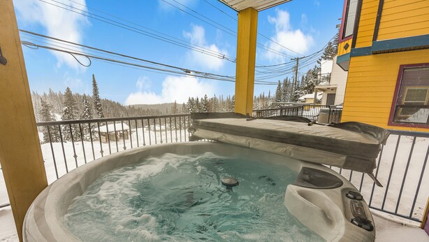 Un bain à remous sur un balcon, avec vue sur des arbres couverts de neige et un bâtiment en arrière-plan.