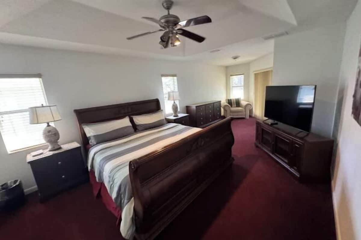 Um quarto com cama, cômoda, televisão e ventilador de teto.