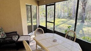 Um quarto com uma mesa e cadeiras, um sofá e janelas amplas com vista para uma floresta.