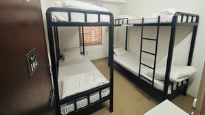 A dormitory room with bunk beds, a door labeled '104,' and a window with blinds. - Travelers Hostel  (Guwahati)