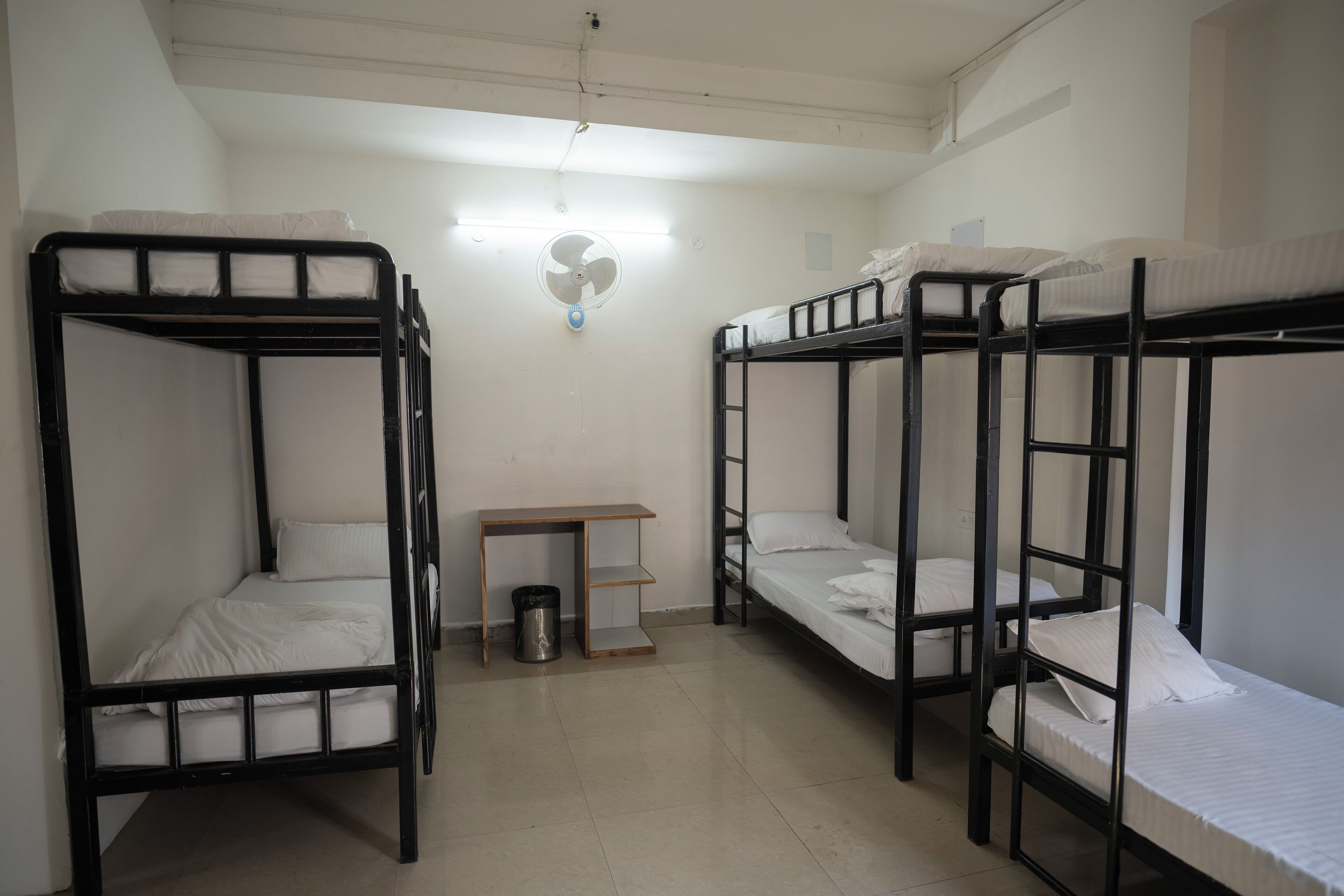 A dormitory room with bunk beds, a desk, and a trash can.