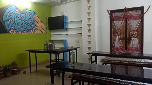 A room with a green wall, a mural, a TV, a window with curtains, and a table with chairs. - Travelers Hostel  (Guwahati)