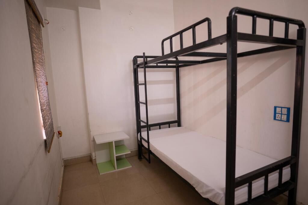 Une chambre avec un lit superposé, une étagère verte et un mur blanc orné d’une enseigne bleue.