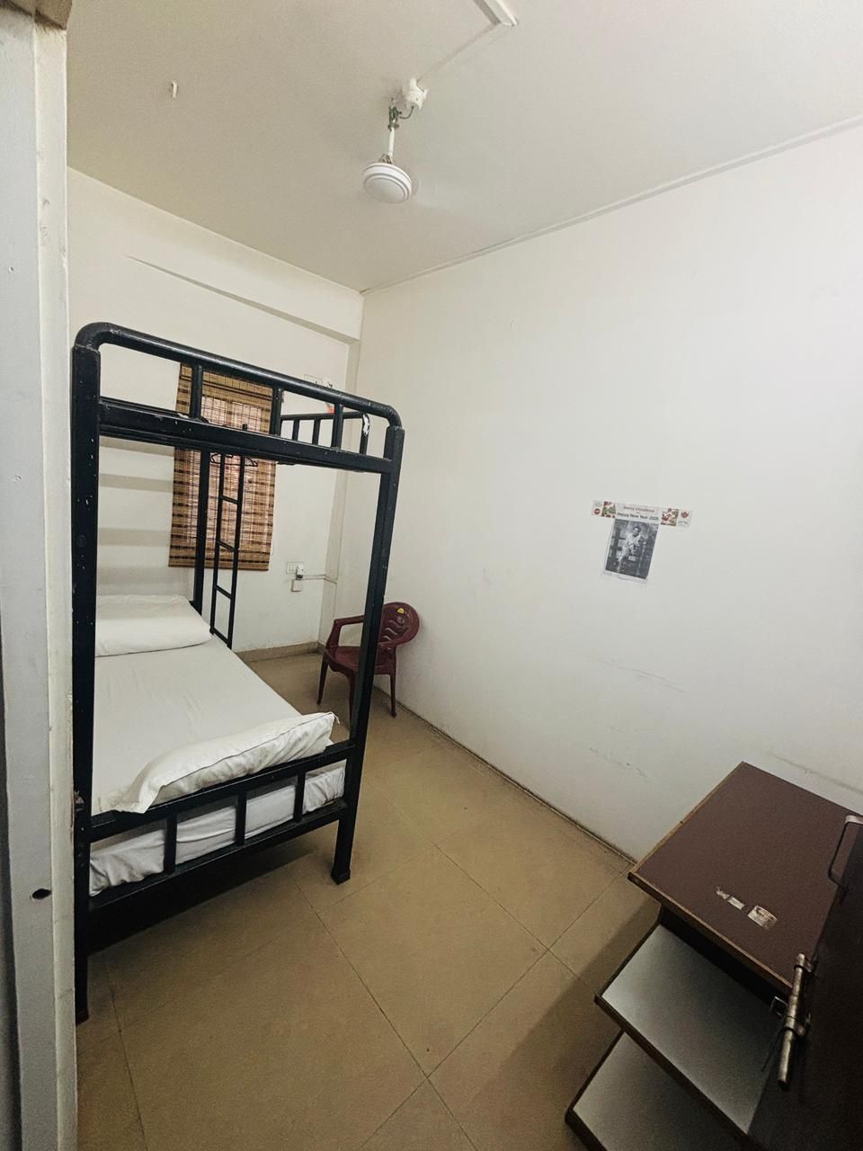 A single bunk bed room with a ceiling fan, a small desk with a chair, and a wall-mounted shelf.