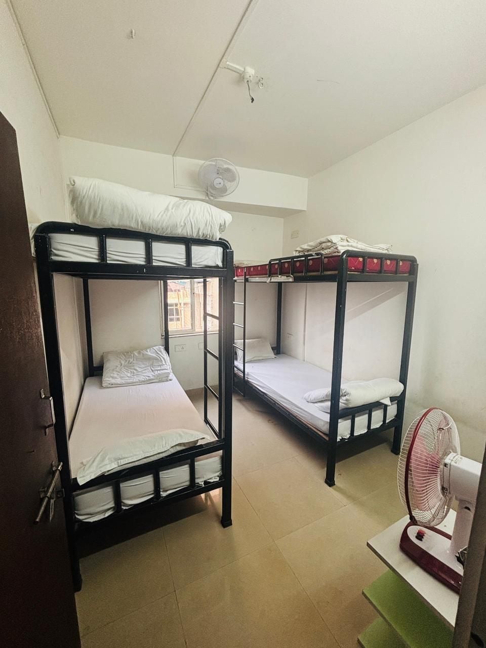 A dormitory room with two bunk beds, a ceiling fan, and a standing fan.