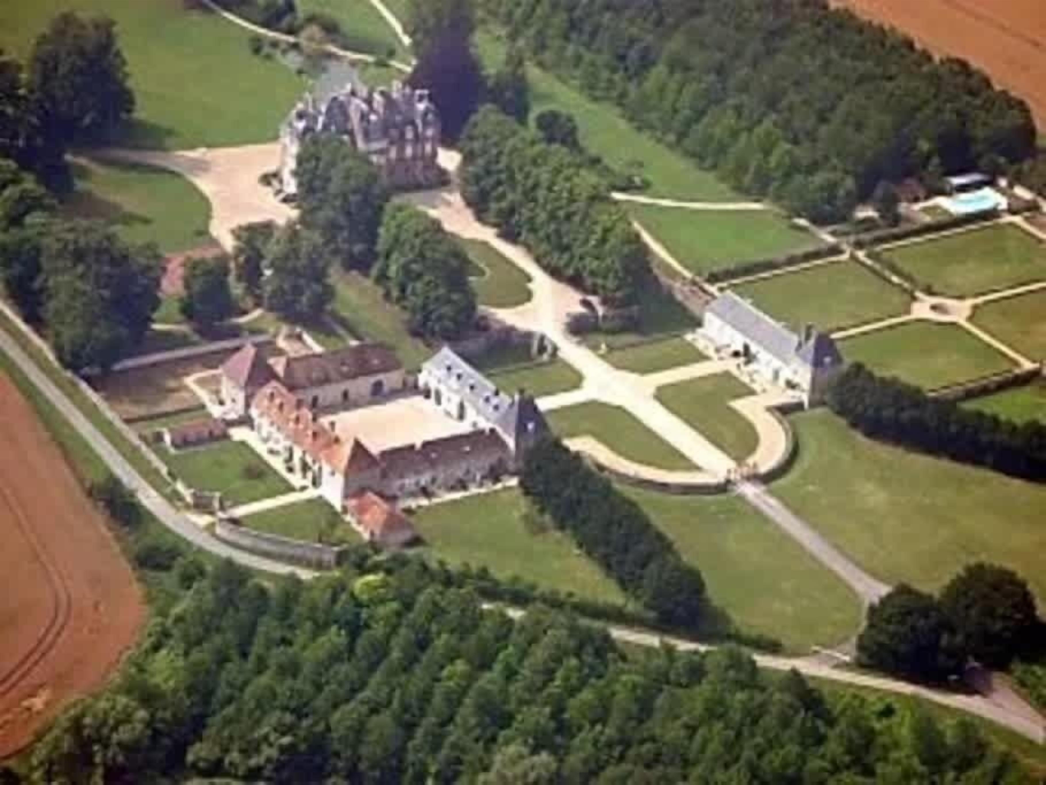An aerial view of a large estate with multiple buildings, including a main house and several smaller structures, surrounded by extensive gardens and pathways.