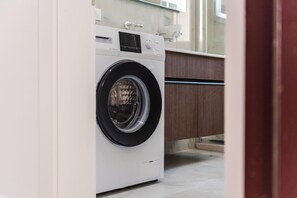 A front view of a compact, modern washing machine in a kitchen with wooden cabinets and a marble countertop. - Beachside Comfort in Orikum (Orikum)
