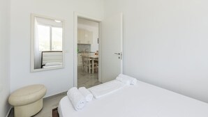 Et minimalistisk hotelværelse med seng, toilet, spejl og en åben dør til et spiseområde.