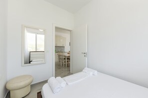 A minimalist hotel room with a bed, a toilet, a mirror, and an open door leading to a dining area. - Beachside Comfort in Orikum (Orikum)