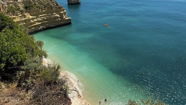 Eine Küstenlandschaft mit Klippen, klarem türkisblauem Wasser und einer fernen Felseninsel.
