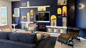 Ein modernes Wohnzimmer mit dunkelblauer Akzentwand, einem Flachbildfernseher, einem Kamin und einer gemütlichen Sitzecke.