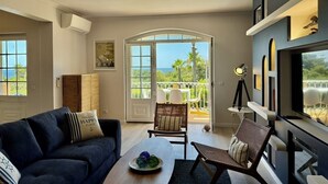 Ein Wohnzimmer mit einer Couch, Sesseln, einem Couchtisch, einem Fernseher und einem Balkon mit Aussicht.