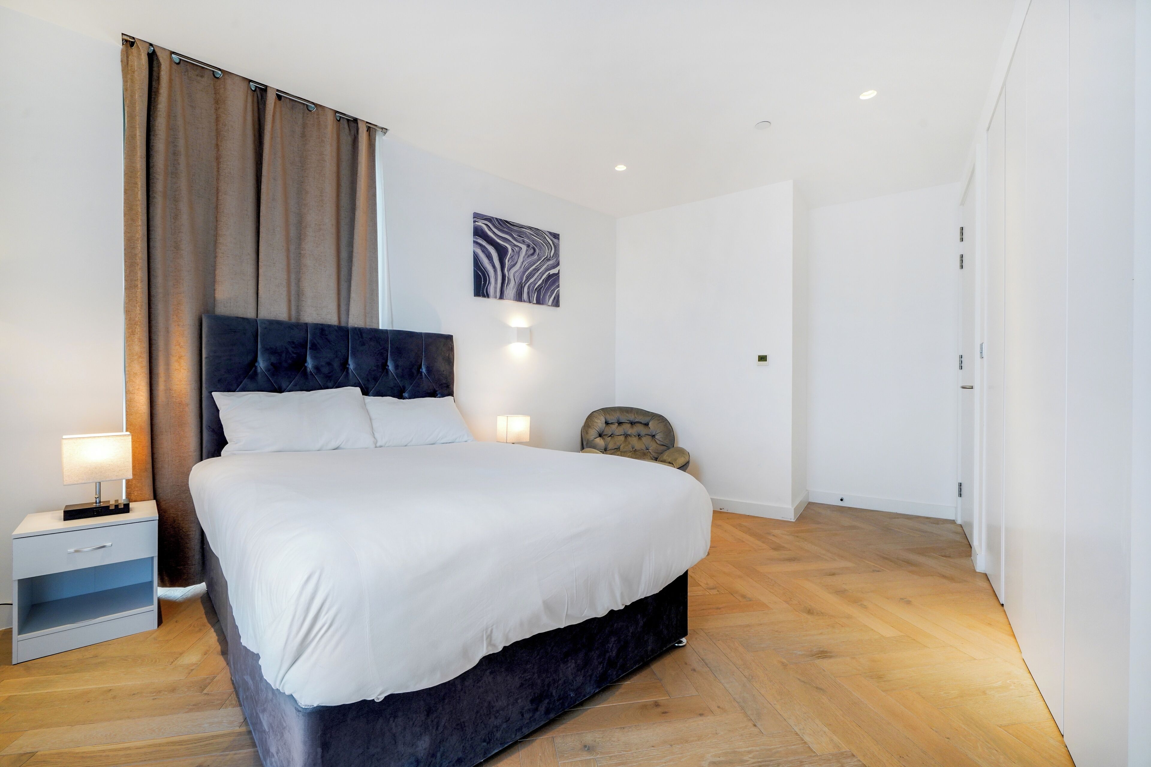 Un dormitorio moderno con una cama grande, una mesita de noche, una silla y una lámpara fijada a la pared.