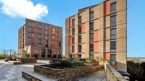 A modern building with a brick facade, multiple windows, and a courtyard with planters. - Cosy London Apartment With 2 Bedrooms (London)