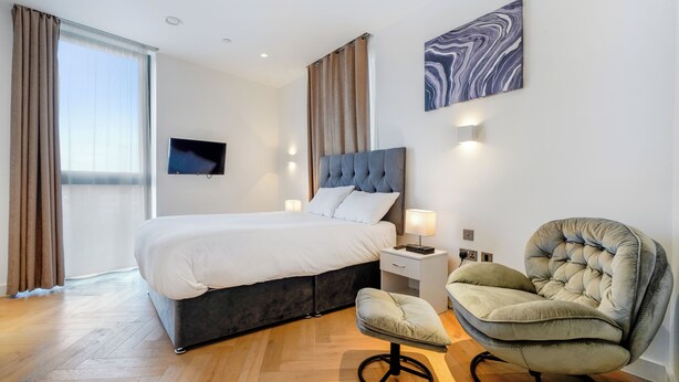 A modern hotel room with a large bed, a television, a chair, and a marble artwork on the wall. - Cosy London Apartment With 2 Bedrooms (London)