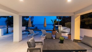 Eine moderne Außenpatio mit Pool, Liegestühlen und Blick auf das Meer im Abenddämmerung.