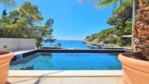 Ein Pool mit Blick auf das Meer und Boote, umgeben von Grünpflanzen und einer Steinmauer.