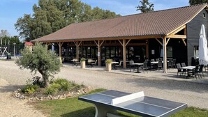 Un espace extérieur aménagé avec des tables et des chaises, une table de ping-pong et un pavillon couvert doté d’un toit en tuiles.