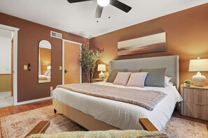 Ein Schlafzimmer mit einem großen Bett, einem Deckenventilator, einem Nachttisch mit Lampe und einem Spiegel an der Wand.