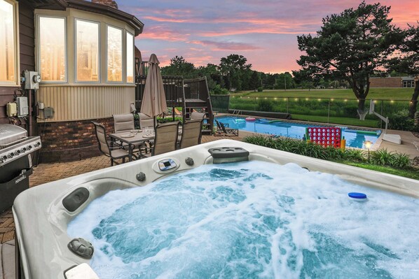 A hot tub with a view of a backyard pool and a house.