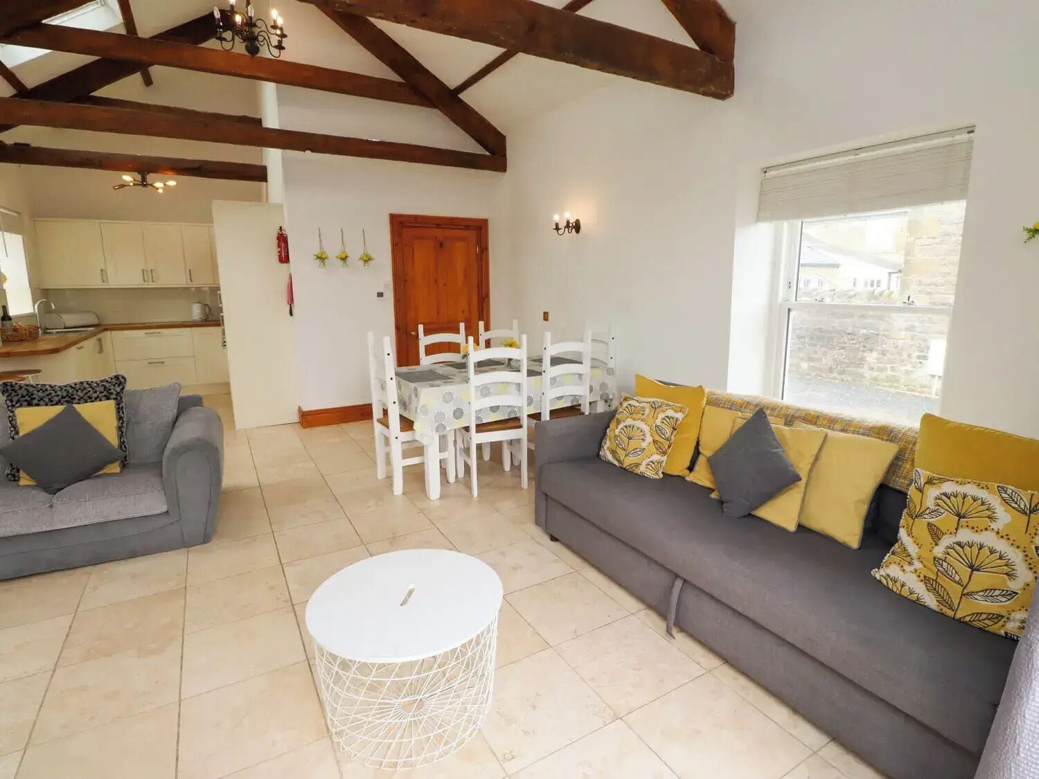 A living room with a grey sofa, a round white table, and a dining area with white chairs.