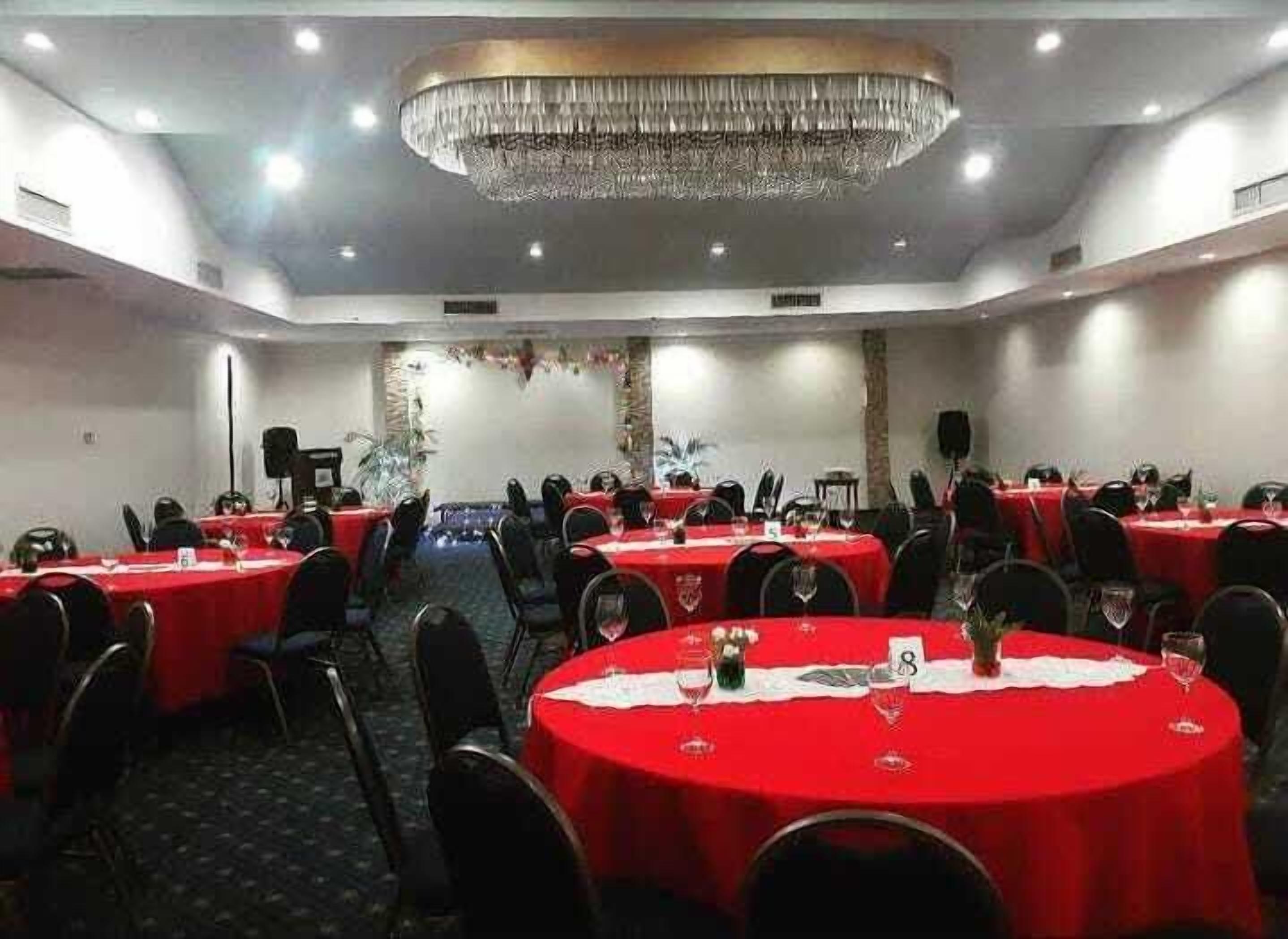 A conference room with round tables covered in red tablecloths, equipped with chairs and wine glasses.