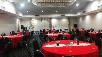 A conference room with round tables covered in red tablecloths, equipped with chairs and wine glasses.