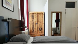 A bedroom with a bed, a wooden wardrobe, a mirror, and a radiator. - Central One-Bedroom Apartment in Konstanz (Konstanz)